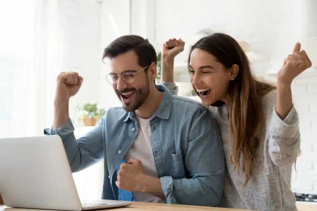 Aufgeregtes junges Paar feiert am Laptop tolles Finanzierungsangebot mit bestem Bauzins.