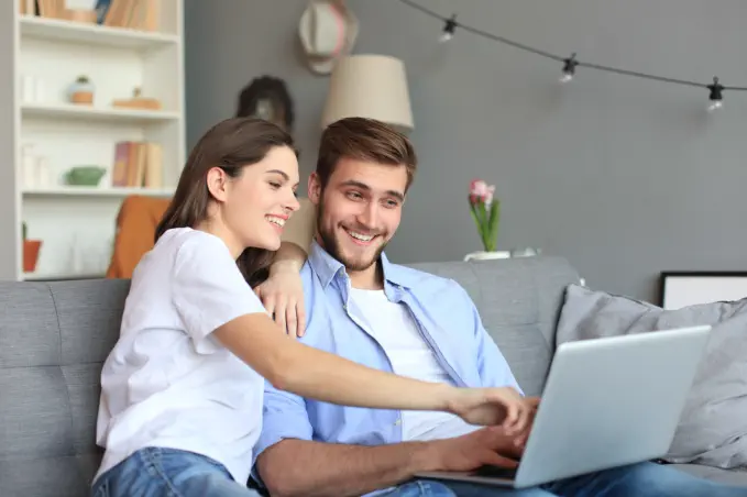 Junges-Paar-benutzt-online-die-Rechner-von-4baufi-Baufinanzierung-fuer-Immobilienbewertung-und-Zinsen-Ihrer-Immobilienfinanzierung-mit-einem-Laptop-auf-dem-Sofa