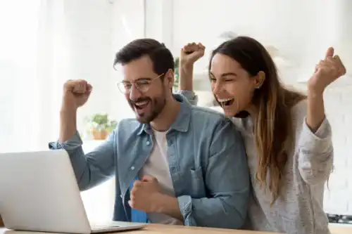 Aufgeregtes-junges-Paar-mit-Laptop-feiern-super-Konditionsangebot-fuer-Ihre-Baufi